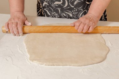 Şef, beyaz ahşap bir masa üzerinde un bulunan ahşap bir iğneyle taze hamuru yuvarlıyor.