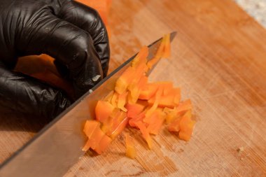 Eldiven giymiş şefin elleri kesme tahtasındaki haşlanmış havuçları kesiyor. Yakın plan. Yemek hazırlama.