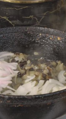 Şef, kızarmış patlıcan parçalarına eski bir dökme demir tavada dilimlenmiş soğan ekler. Yakın plan.