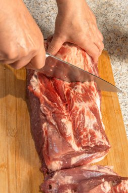 Bir aşçının eli pişirmek için çiğ domuz boynunu bıçakla keser. Yakın plan.