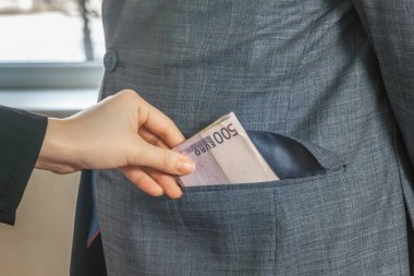 El, önünde duran takım elbiseli ve kravatlı bir adamın cebine Avrupa para birimi banknotları atıyor. Rüşvet vermek için. Yozlaşma