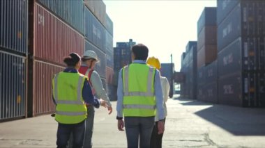 Bir grup iş adamı depoda konuşuyor. Erkek ve kadın mühendis işçiler güvenlik kaskı, yelek ve nakliye için kargo kutusunun listesini ve envanterini giyerler.