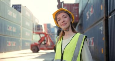 Üniformalı ve koruyucu kasklı çekici bir mühendis kadının portresi gülümsüyor ve fabrika deposundaki kameraya bakıyor.