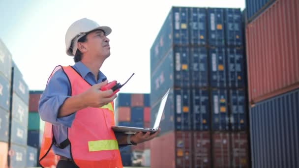 一位身穿硬帽和安全背心的亚裔工头就用无线电控制集装箱装运货物问题进行了会谈 — 图库视频影像