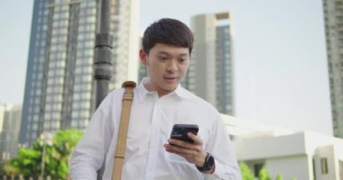 Mutlu Asyalı işadamının portresi akıllı telefondan başarıya ulaşırken açık alanda inşaat başarısı, modern şehirde zaferi telefonla kutlarken, ağır çekimde....