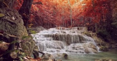 Beautiful waterfall with trees, red leaves, rocks and stones in autumn forest