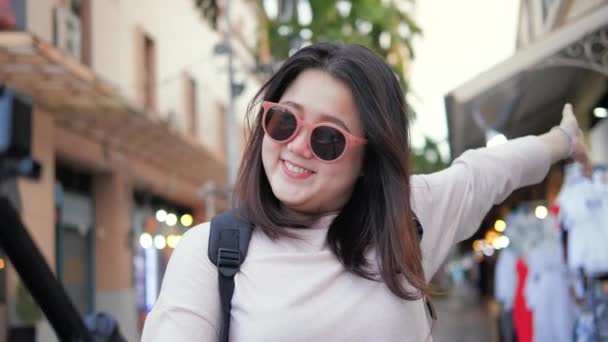 バンコクの市場で休暇の週末の場所を示すために陽気な動きでカメラを持つ旅行者アジアの女性タイ — ストック動画