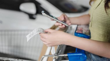 Kadınlar süpermarketten alışveriş yaptıktan sonra fatura hesaplamak için cep telefonu kullanıyor, uzun market makbuzlarını elle kontrol etmek için, bütçe ve tasarruf uygulaması kullanıyor