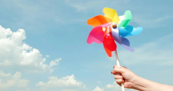 Renkli fırıldak hareketi bulanıklaştı. Mavi gökyüzü arka planında renkli plastik yel değirmenleri tutan kadın. Yeşil enerji kavramı