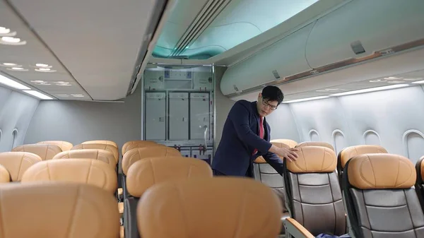 乘客到达目的地并下机后 身穿制服的亚洲男性空姐正在检查飞机座位 — 图库照片
