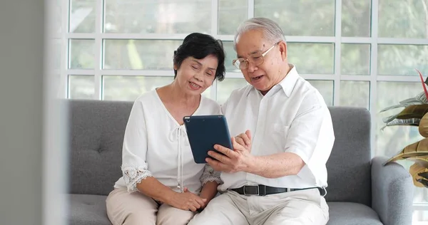 Lykkelig Smilende Asiatisk Eldre Par Som Snakker Nettbrett Mens Sitter – stockfoto