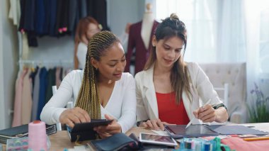 İki profesyonel Asyalı ve Afro-Amerikalı kadın moda tasarımcısı. Tablet tarama desenleri kullanıyorlar.