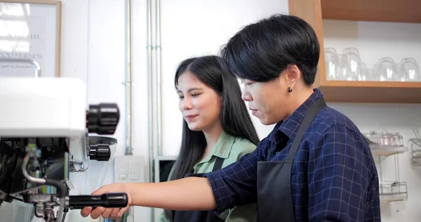两名身穿围裙的亚洲妇女在咖啡店里谈论并教授如何使用咖啡机 — 图库照片