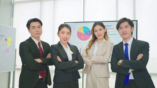 オフィスでカメラと腕を見て立ってスーツを身に着けている若いプロのアジアのビジネスのグループ — ストック写真