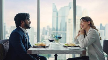 Mutlu iş çifti konuşuyor ve restoran ve şehir manzarasında yemek yiyip şarap içiyor.