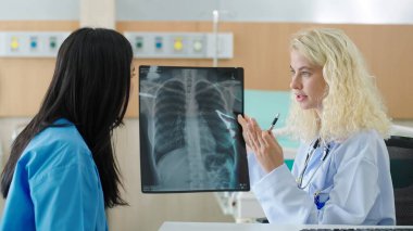 Klinikteki enfeksiyonun neden olduğu akciğer zatürresi olan röntgen filmi hakkında kadın doktorla konuşan profesyonel bir beyaz kadın. Covid-19 xray testi, covid dünya çapında virüs salgını