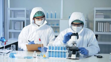 Biyolojik tehlike koruma giysileri içinde Asyalı doktor laboratuarda mikroskop ve aşı araştırmalarında virüs örneğini analiz ediyor. Karantina veya virüs salgını kavramı