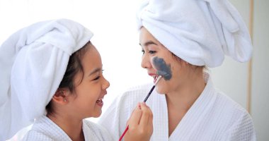 Kızı, duştan sonra yatak odasında eğlenirken annesinin yüzüne gri maske kremi sürmüş. Aile güzelliği