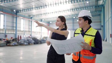 Profesyonel Asyalı erkek mimar elinde fabrika tasarımının planlarını tutuyor fabrika endüstrisinde kadın yöneticiyle konuşuyor.