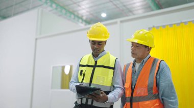 Güvenlik kaskı takan iki profesyonel fabrika işçisi depoda çalışırken tablet kullanıyorlar.