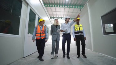 Depoda yürüyen ve iş için konuşan bir grup fabrika çalışanı. Depoda güvenlik kaskı denetimi yapıyorlar.