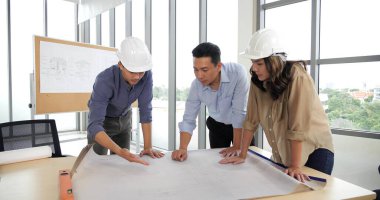 Ofisteki yönetim kurulu masasının planları üzerinde çalışan Asyalı grup mimarları, iş planlarını tartışan mimarlar.