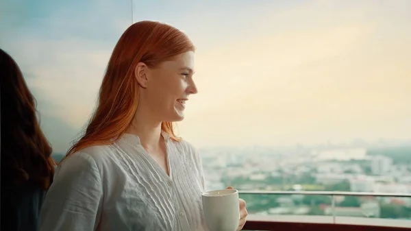 若い美しい女性がカップを持っているお気に入りのお茶を楽しむ朝はバルコニーで街の景色を見ながら爽快な — ストック写真