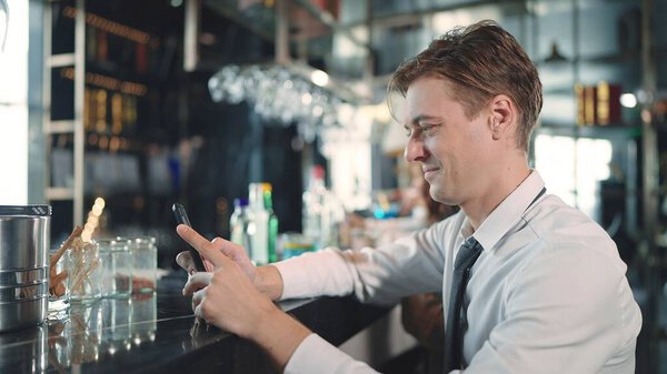 A young businessman sitting and using smartphone for chatting at the bar in the restaurant