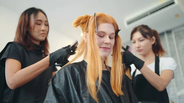 Two asian woman hairdressers with black apron are coloring customer hair with brushes in a hair salon