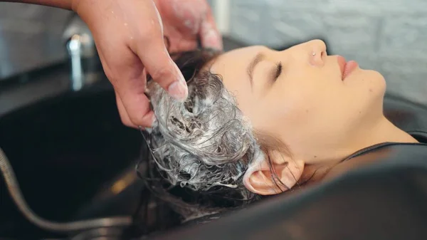 Profesyonel bir güzellik salonu çalışanı müşteri saçlarını yıkıyor. Şampuanla temizle ve kuaförde saçına saç kremi sür.
