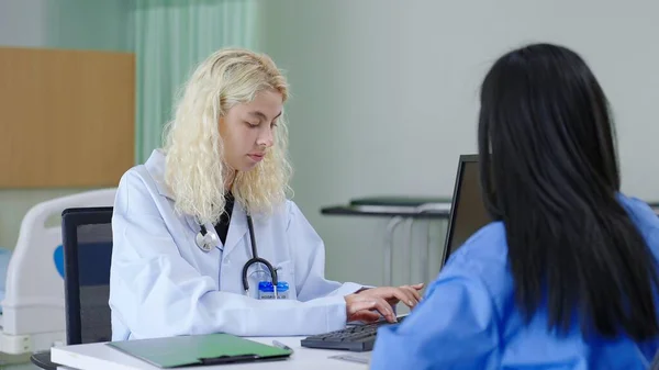 白衣を着た女性医師が働き 医療室のノートパソコンのキーボードに患者の履歴を入力する — ストック写真