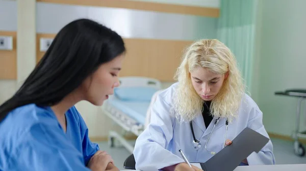 女性の医療活動は 病院のテーブルの上に処方を書きます 病院の治療室に座っている患者 — ストック写真