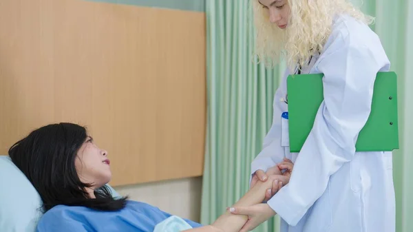 アジア女性患者手首の白人女性医師ホールドは 診療所や病院でベッドの上に横たわるパルスを測定します — ストック写真