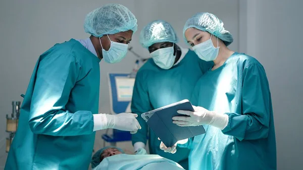 在手术室现代医院急诊科 专业的外科医生和辅助人员在手术过程中交谈和使用数字平板电脑 — 图库照片