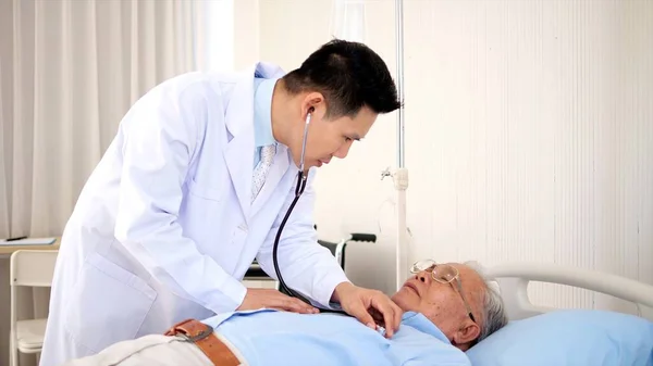 Asian male doctor using stethoscope to listen to lung and heart sound of asian elderly man pateint who is sick and lying in hospital bed. older people healthcare support concept