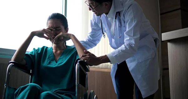 坐在轮椅上的年轻的沮丧的亚洲女人闭上了眼睛 哭泣着 医生在医院里讲话 安慰和鼓励 — 图库照片