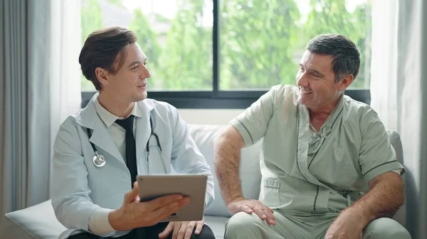 デジタルタブレットを使用して若い医師は治療後の患者に症状を説明するか 病院の老人患者と話す — ストック写真