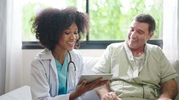 アフリカ系アメリカ人女性医師は デジタルタブレットを使用して 治療後の患者への症状を説明するか 病院の老人患者と話をした — ストック写真