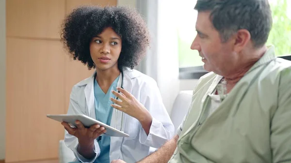 アフリカ系アメリカ人女性医師は デジタルタブレットを使用して 治療後の患者への症状を説明するか 病院の老人患者と話をした — ストック写真