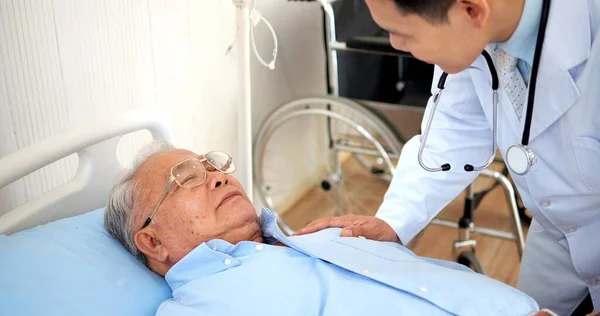 アジアの医師とともに聴診器ケア高齢者でベッドで病院 — ストック写真