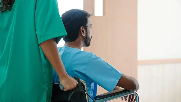 病院の治療室に行くインド人男性患者の車椅子を押す看護師の背景 — ストック写真