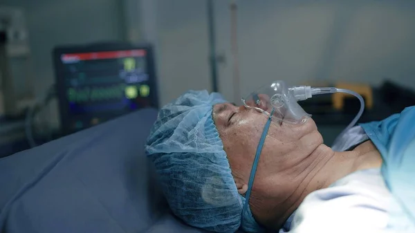 在手术室的手术床上躺着医用通风机时 将病人的脸关闭 模糊的背景显示病人的心率 — 图库照片