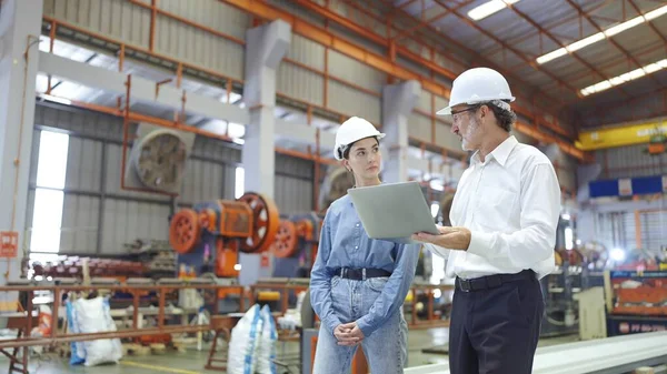 Two professional engineer man and woman manager leader wearing helmet and holding laptop walking in factory talking and discussing for work