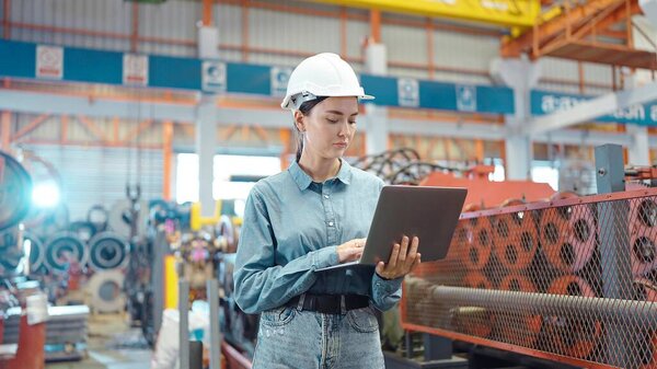 Engineer manager leader woman wearing helmet holding laptop standing and check in workplace area at manufacturing factory. Factory and Industrial plant concept