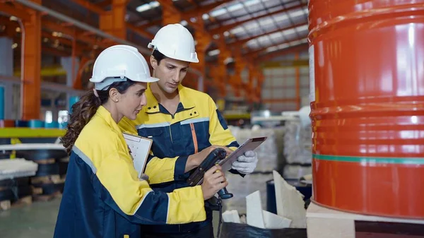 Two factory workers man and woman in uniform using barcode scaner and tablet for working checking stock at industrial warehouse