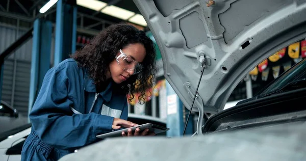 女性の機械工は診断ソフトウェアの点検車エンジンのタブレットコンピュータを使用する 専門家は エンジンベイ内の壊れたコンポーネントを見つけるために車を検査します レンタカーサービス — ストック写真