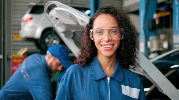 制服姿でラテン女性の車の整備士の笑みを浮かべて顔カメラで自動車 — ストック写真