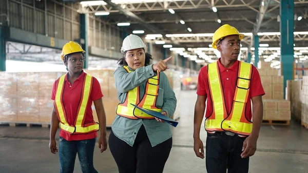 Young African American black workers with list checking stock condition in business factory industry warehouse wearing engineer suit and helmet for safety. Logistic industry concept