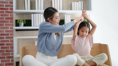 Mutlu Asyalı anne ve kızı evde yoga yapıyor. Asma suratlı, kol dengesini koruyor. Aile oturma odasındaki kanepede lotus pozisyonunda oturur. Aile yogası