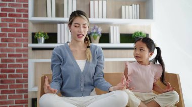 Mutlu Asyalı anne ve kızı evde yoga yapıyor. Asma suratlı, kol dengesini koruyor. Aile oturma odasındaki kanepede lotus pozisyonunda oturur. Aile yogası